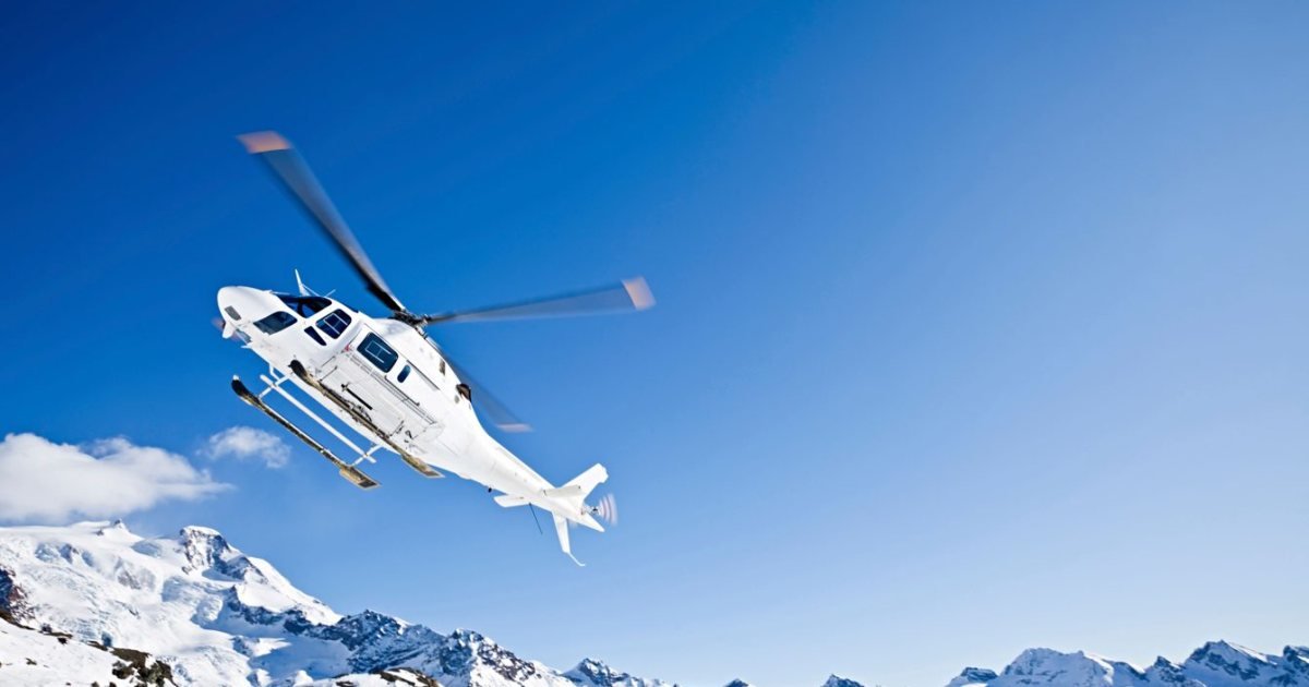 Twin-engine helicopter climbing over snow-covered peaks